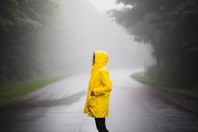 黄色いレインコートを着て雨の道を歩く人